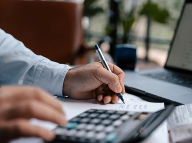 Free A person calculating finances with a calculator and pen on a desk indoors. Stock Photo